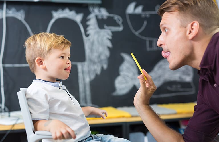 therapist holding a tongue depressor up to a little boy